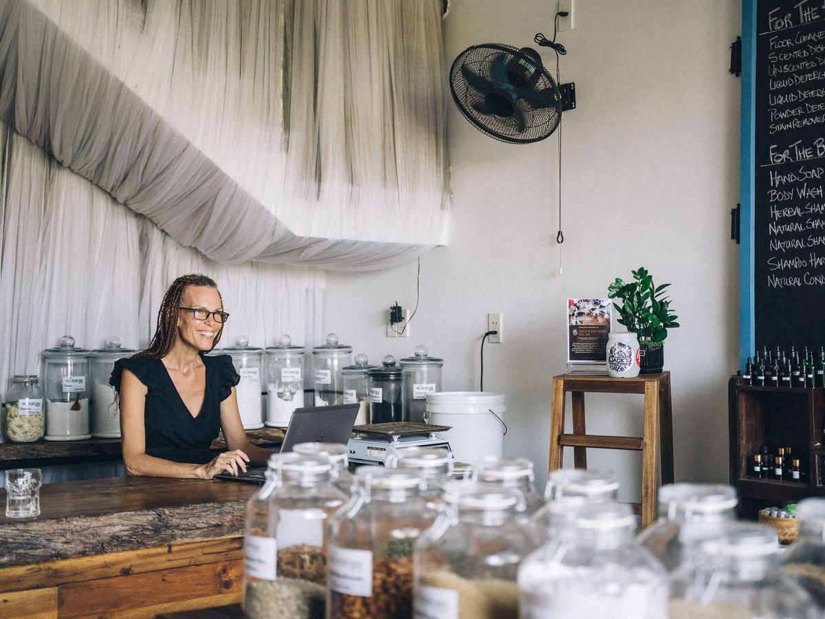 A shop owner working on a laptop behind the counter of a small store