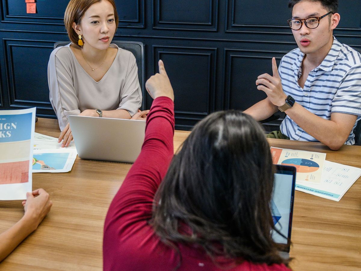 A team meeting around a table with laptops in front of a wall of colorful sticky notes